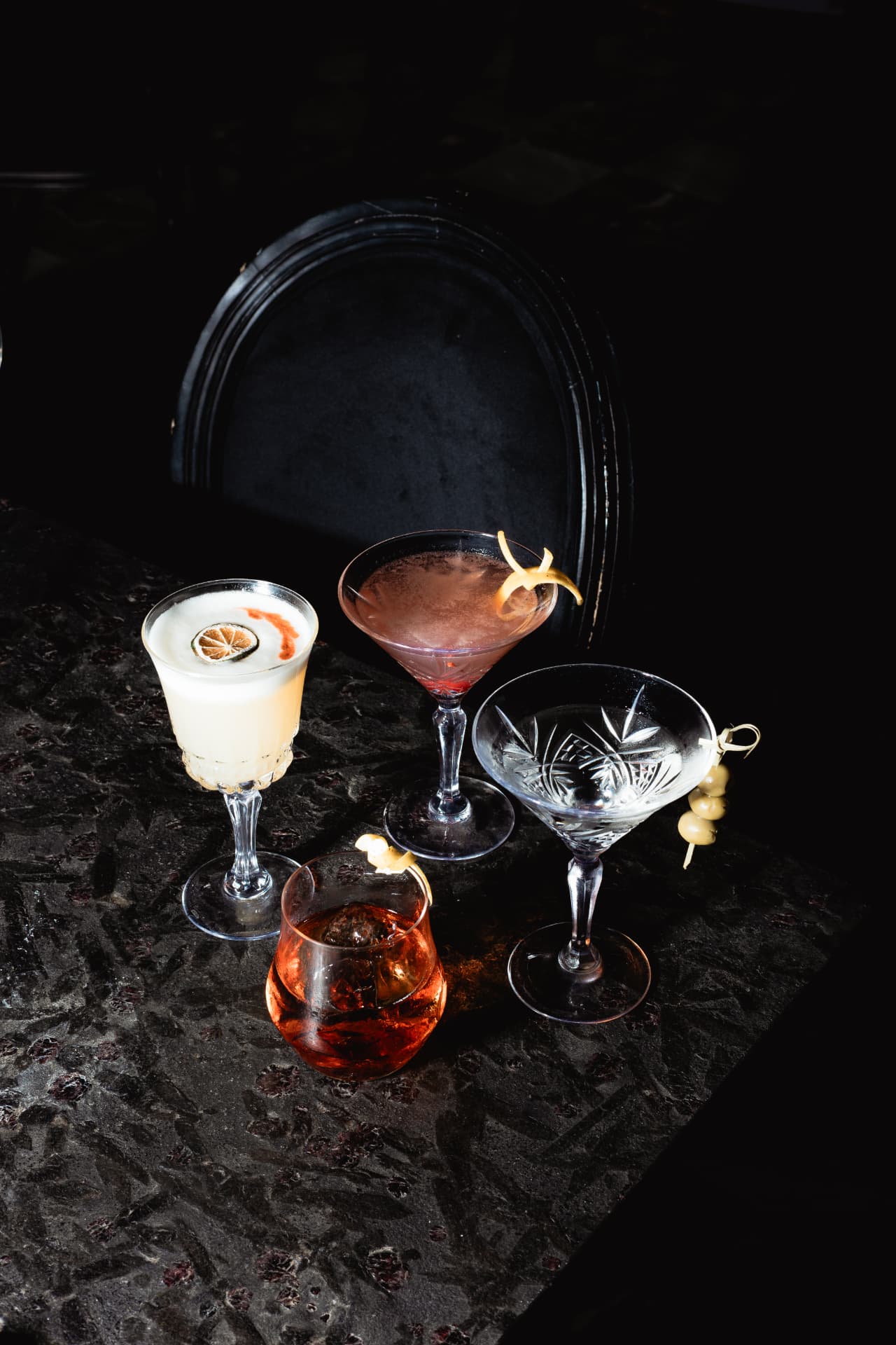 A selection of classic cocktails served in coupes on a dark table